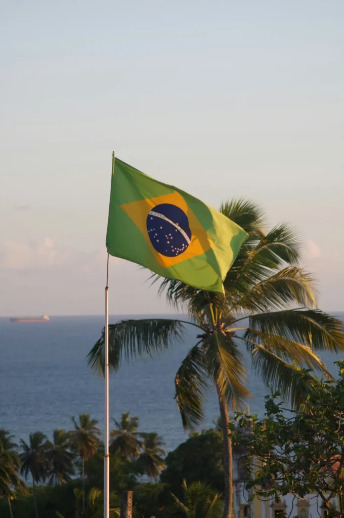 Drapeau brésilien flottant au vent avec la mer en arrière-plan, symbolisant le visa longue durée au Brésil